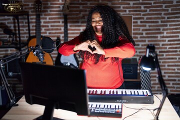 Plus size hispanic woman playing piano at music studio smiling in love doing heart symbol shape with hands. romantic concept.