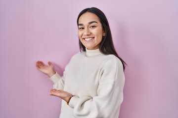 Young south asian woman standing over pink background inviting to enter smiling natural with open hand