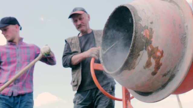male builders load sand into a concrete mixer.