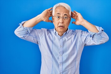 Hispanic senior man wearing glasses crazy and scared with hands on head, afraid and surprised of shock with open mouth