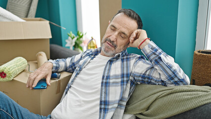 Middle age man holding smartphone sitting on sofa sleeping at new home