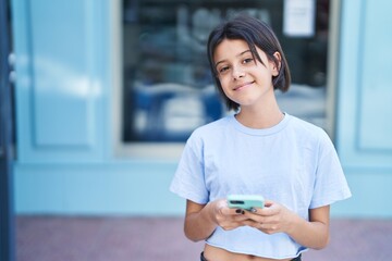 Adorable hispanic girl smiling confident using smartphone at street