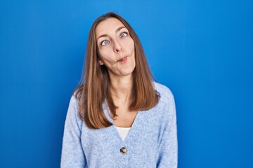 Young woman standing over blue background making fish face with lips, crazy and comical gesture. funny expression.