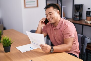 Fototapeta premium Young chinese man business worker talking on smartphone reading document at office