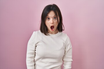 Woman with down syndrome standing over pink background in shock face, looking skeptical and sarcastic, surprised with open mouth © Krakenimages.com