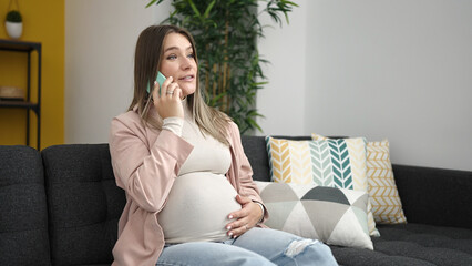 Young pregnant woman talking on smartphone touching belly at home