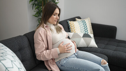 Young pregnant woman touching belly with relaxed expression at home