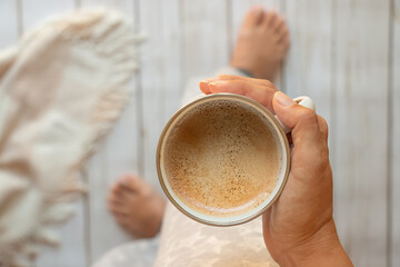 taza de café con espuma en manos de una mujer, vista cenital - obrazy, fototapety, plakaty