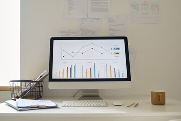 Computer with financial graphs on monitor standing on table in office