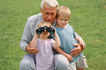 Grandfather and grandchildren using binoculars In Park. Happy family time. Old man grandpa playing...