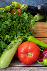 Various vegetables on a wooden table. Tomato, Green Pepper, Red Pepper, Parsley, Carrot, Eggplant, Cucumber, Zucchini.
