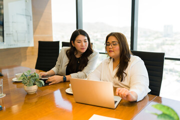 Two businesswomen looking at laptop and discussing in meeting room