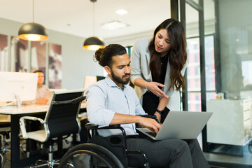 Businesswoman discussing work with a disabled businessman using laptop in office