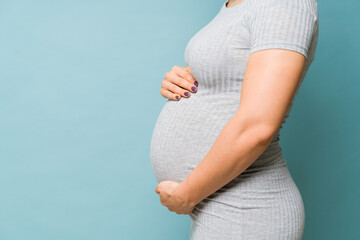 Closeup of a pregnant woman embracing her belly in a studio with plenty of copy space - obrazy, fototapety, plakaty