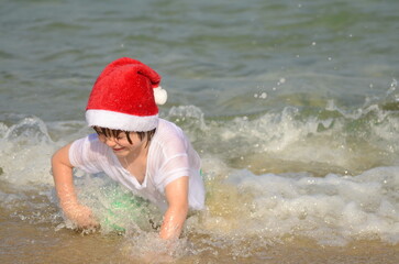 Cute boy in santa hat on the beach. The concept of vacation at sea, family holidays in December. Child on vacation.