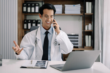 Male doctor talking on mobile phone and working with laptop computer.