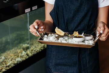 Female hands holding Fresh oysters with lemon. raw opened oyster, lifestyle food, ready to eat. Oyster dinner with champagne in restaurant