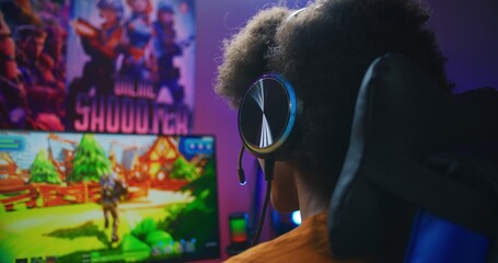 African American gamer plays in third person shooter on PC at home. Computer monitor with displayed...