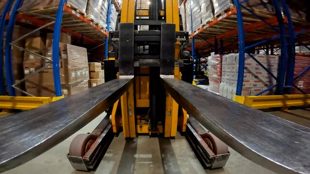 The load lifter rides on the warehouse pov. Forklift fork close-up. Modern forklift in a large warehouse