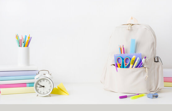 School supplies and backpack on table over white wall background