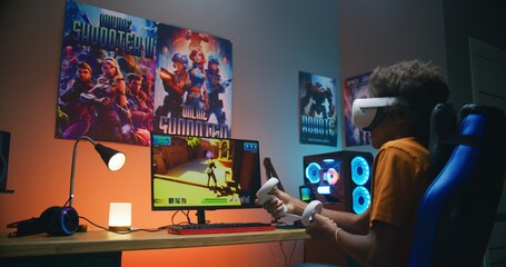 African American teenage gamer in VR headset plays virtual third-person 3D shooter on personal computer using wireless controllers. Video game online streaming or esports tournament. Gaming at home.