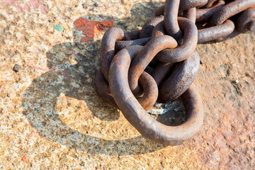 Detail of an old rusty metal chain anchored to a concrete block