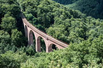 Fototapeta na wymiar old arch Bridge railway viaduct between hills in the green Forest Germany trees