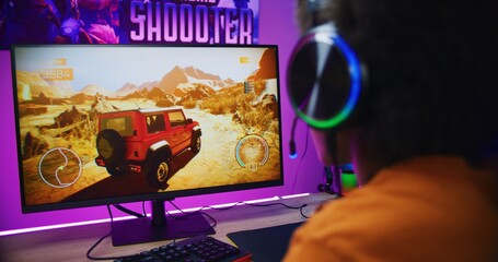 African American teenager in headphones plays in online 3D racing game on modern powerful computer...
