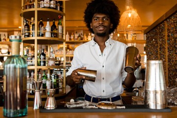 young and happy latin bartender with curly hair starting to prepare a cocktail