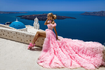 Glamour, stylish elegant bride woman in pink long wedding dress is posing near Church of the Three Bells in Fira in Santorini. - obrazy, fototapety, plakaty