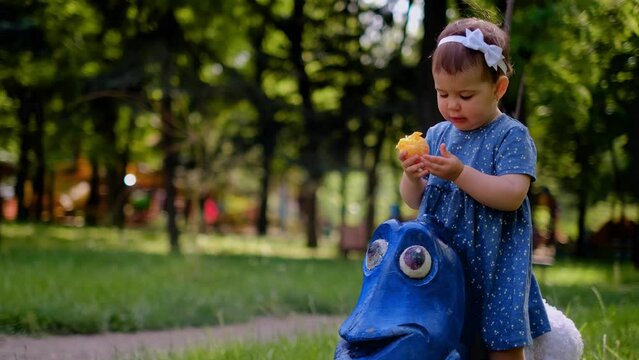 A small child sits on a swing in the playground, eats an orange, the use of vitamins for children, children's multivitamins, orange juice flows down the arm, a swing in the form of a blue fish