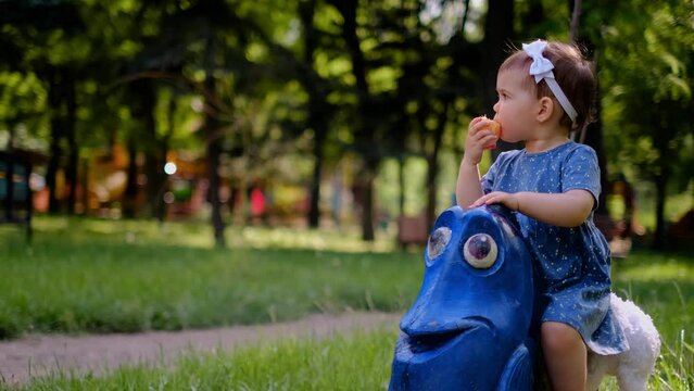 A small child sits on a swing in the playground, eats an orange, the use of vitamins for children, children's multivitamins, orange juice flows down the arm, a swing in the form of a blue fish