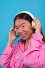 smiling asian girl looking at the camera while listening to music with wireless headphones