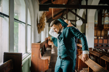 The groom carefully pulls on a green jacket as he prepares for the upcoming wedding ceremony,...