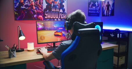 Young gamer plays in car racing simulator on PC at home. Computer monitor with displayed online video game live stream or cybersport championship. Desk illuminated by RGB LED strip light. © Framestock
