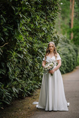 Obraz na płótnie Canvas A beautiful bride with a long dress stands in nature in the green with a large bouquet. Wedding portrait of a young bride. Wedding photography.