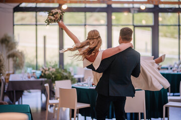 The groom carries the bride in his arms into the celebration hall