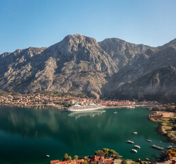 Aerial panoramic view of the picturesque town of Kotor with beautiful coastline, promenade, red roofs, marina with boats and big cruise ship, Montenegro