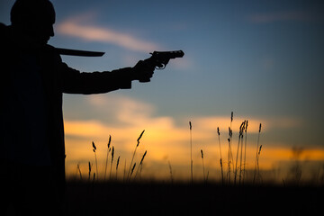 Silhouette of a demon and vampire hunter with a dramatic sky in the background. A man with a katana and a revolver. Fantasy and halloween concept