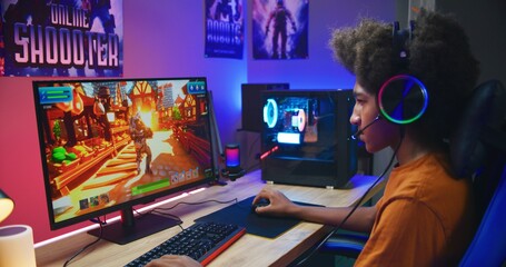 African American gamer plays in third person shooter on PC at home. Computer monitor with displayed...