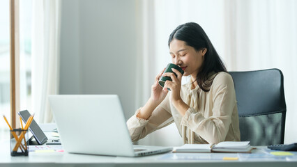 Attractive young businesswoman drinking coffee and working at modern office.