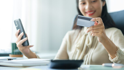 Smiling young woman using smart phone and holding credit card for shopping online.