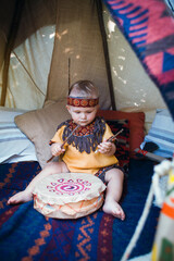 Little Boy in Indian Clothes Playing on Tam Tam in Wigwam © andrii_popovych
