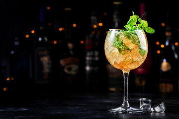 Summer refreshing alcoholic cocktail drink with cognac, liqueur, prosecco or sparkling wine with ice and mint in wine glass, dark background, bar tools and bottles