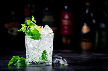 Tommy's margarita alcoholic cocktail drink with tequila, lime juice, syrup and ice in rocks glass, dark background, bar tools and bottles