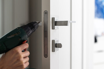 A locksmith is repairing an interior door lock. Close-up of male hands repairing or replacing an entrance door lock with a hex screwdriver