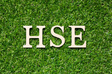 Wood alphabet letter in word HSE (Abbreviation of Health, safety, environment) on artificial green...