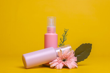 Two cosmetic bottles decorated with flower on yellow background. Natural extract for organic cosmetic concept.