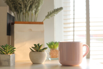 Pink coffee cup with small succulents plants on the table near window with the morning sun light