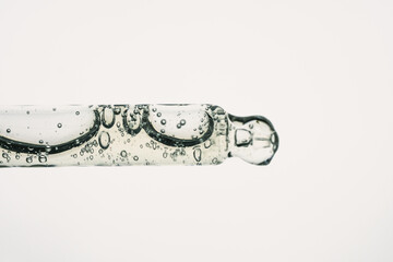 Glass pipette with cosmetic liquid or polyglutamic acid with air bubbles on white background. Side...